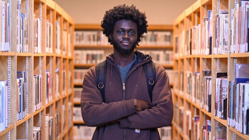 Student standing upfront in the middle of a book aisle at KCC Library. 